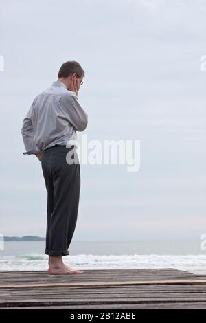 Un uomo d'affari pensoso che si trova a piedi nudi sulla spiaggia Foto Stock