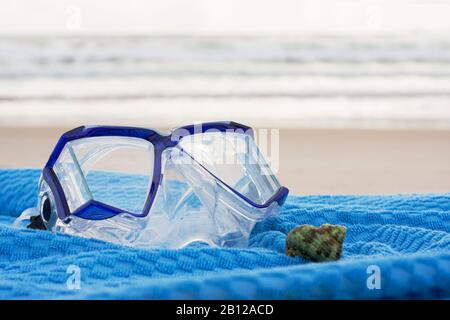 Maschera subacquea una conchiglia adagiata su un asciugamano blu su una spiaggia soleggiata Foto Stock