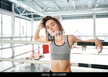 Bella giovane sportswoman in tuta grigia in piedi da pugilato anello Foto Stock