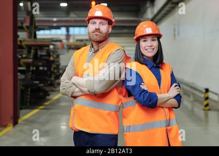 Due giovani ingegneri di successo in hardhats e abbigliamento da lavoro arancione Foto Stock