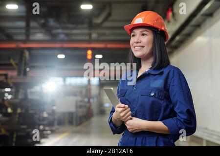 Allegro giovane femmina wngineer con touchpad in piedi in officina Foto Stock