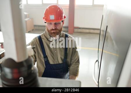 Giovane ingegnere serio con barba davanti al pannello di controllo in officina Foto Stock