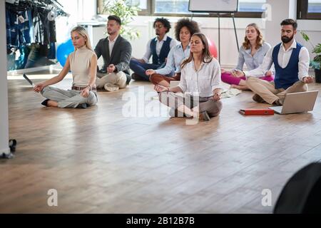 colleghi d'affari che meditano al lavoro, seduti sul pavimento; copiare spazio. moderno, business, concetto di meditazione Foto Stock