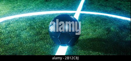 Campo da calcio neon con palla su linee incandescenti su un campo verde erboso di notte in un panorama banner con spazio copia per lo sport o il tema del calcio Foto Stock