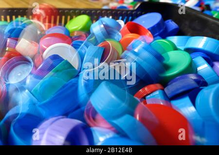 Tappi in plastica per bottiglie di bevande di varie dimensioni e colore che cadono nel cestello. Foto Stock