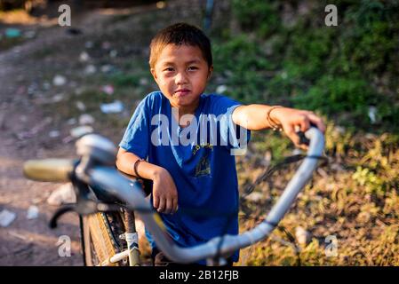 Laotiani del ragazzo con la sua bicicletta in un villaggio in Laos Foto Stock