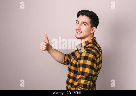 come. bel giovane brunetta che mostra il pollice grande su contro lo sfondo rosa pastello Foto Stock