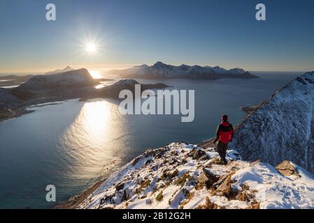 Dal vertice di Mannen, escursionista si affaccia sul paesaggio delle Lofoten verso il sole, Lofoten, Nordland, Norvegia Foto Stock