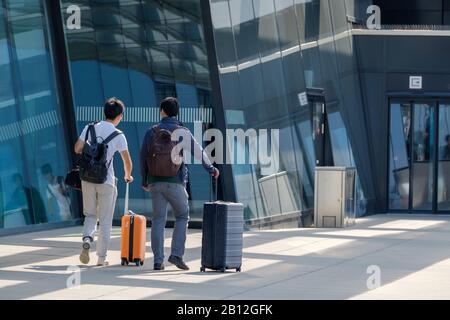 Due viaggiatori vanno all'ingresso dell'aeroporto con valigie Foto Stock