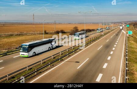 Caravan o convoglio di Quattro autobus bianchi in linea che viaggiano su un'autostrada di campagna sotto il cielo blu stupefacente. Highway scuola bambini trasporto con bianco Foto Stock