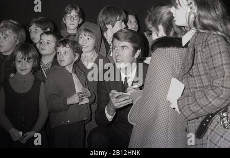 1960s, storico presentatore e intrattenitore della televisione britannica, Leslie Crowther in un fete di carità, circondato dai bambini mentre firma autografi, Londra, Inghilterra, Regno Unito. Era conosciuto tra i giovani per la presentazione di programmi tv per bambini come 'Crackerjack' e 'Meet the Kids' e radio show, 'Junior Choice'. Foto Stock