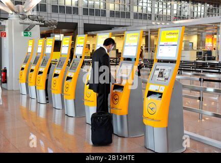 Terminali di check-in automatizzati da Lufthansa e un giovane uomo d'affari, sicuro di sé, che indossa un abito e un bagaglio per un viaggio d'affari all'Aeroporto di Amburgo, Amburgo, Germania, Europa Foto Stock