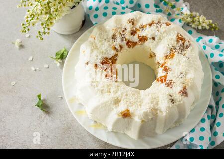 Dessert di Pannacotta. Cottage souffle di formaggio panna cotta con albicocche e decorazioni di cocco su una pietra o ardesia su un piano di lavoro leggero. Spazio di copia. Foto Stock