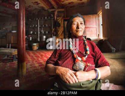 Una casalinga tibetana nella sua casa tradizionale indossando gli accessori tradizionali della sua tribù, altopiano tibetano Foto Stock