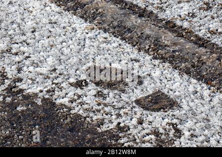 L'ingombro lasciato da uno stivale è rimasto impressionato da una neve ghiacciata su un terreno sottile in un parcheggio. L'asfalto pavimentato è visto al suo interno, un Foto Stock
