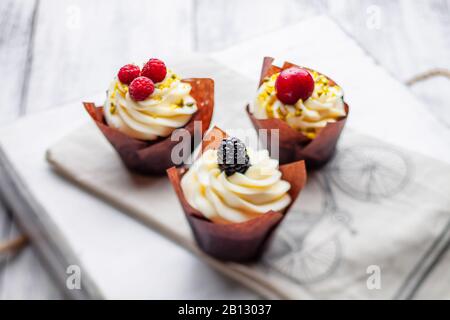 Muffin con cioccolato belga e crema di cioccolato bianco e mascarpone con frutti di bosco su un vassoio di legno Foto Stock