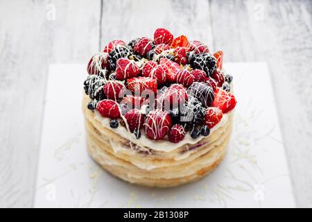 torta di frittelle con un berretto di frutti di bosco in salsa di cioccolato bianco su un tavolo bianco di legno Foto Stock