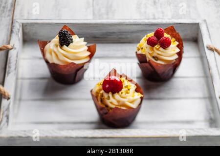 Muffin con cioccolato belga e crema di cioccolato bianco e mascarpone con frutti di bosco su un vassoio di legno Foto Stock