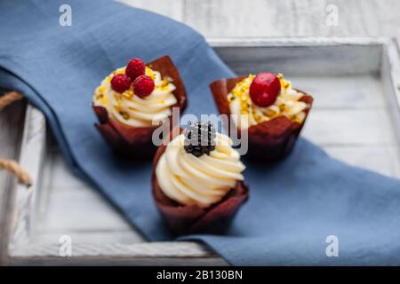 Muffin con cioccolato belga e crema di cioccolato bianco e mascarpone con frutti di bosco su un vassoio di legno Foto Stock