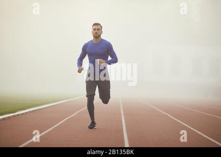 Un giovane atleta corre su uno stadio nella nebbia.