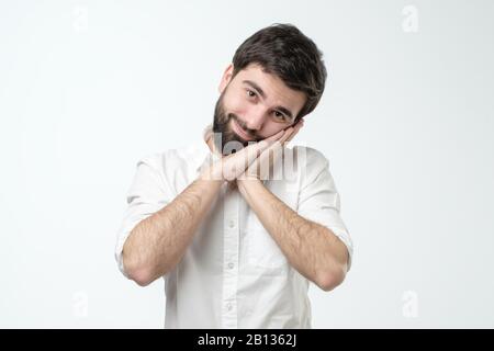 Uomo ispanico che indossa camicia bianca dormire stanco sognare e posare con le mani insieme sorridente. Studio Foto Stock