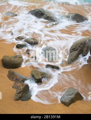 Le onde si infrangono su una costa rocciosa e frastagliata in una mattinata travagliata. Foto Stock