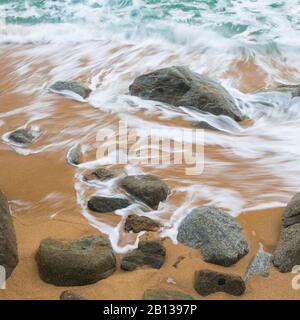 Le onde si infrangono su una costa rocciosa e frastagliata in una mattinata travagliata. Foto Stock