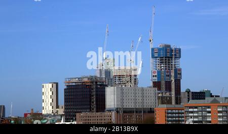 Alti edifici, tra cui alcuni in costruzione con gru a torre, nel centro di Manchester, Regno Unito, con un cielo blu oltre. Foto Stock
