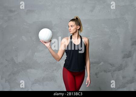 Pallavolo ragazza tenere e calcio palla in costume nero su sfondo grigio muro in cemento Foto Stock