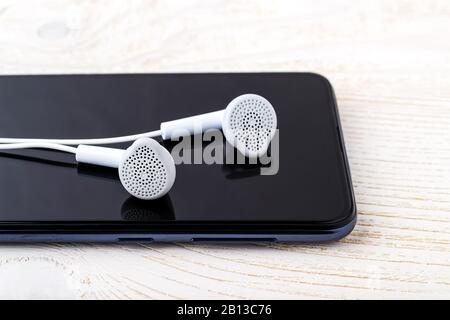 Primo piano degli auricolari bianchi su uno schermo nero dello smartphone. Ascolta la musica. Moderno dispositivo personale con touchscreen per musica e comunicazioni. Foto Stock