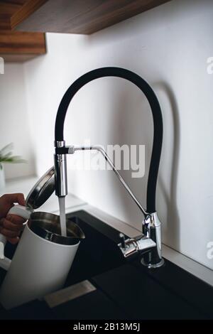 Immagine verticale del bollitore elettrico con la mano dell'uomo e la parte superiore aperta e versare acqua dal rubinetto. Necessità di scaldare su acqua. Cucina moderna con Foto Stock