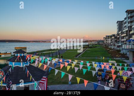 Mt Rainier aleggia sopra il centro cittadino di Tacoma e inizio Bay come si vede dal punto Ruston con la gente a piedi e in bici di equitazione Foto Stock