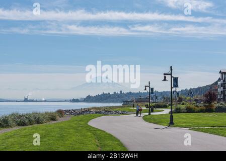 Mt Rainier aleggia sopra il centro cittadino di Tacoma e inizio Bay come si vede dal punto Ruston con la gente a piedi e in bici di equitazione Foto Stock