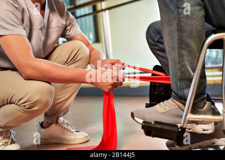 giovane fisioterapista asiatica che lavora con l'uomo anziano per aumentare la forza della gamba usando la banda di resistenza Foto Stock