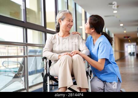 personale cordiale che si prende cura di casa di cura parlando con la donna asiatica senior in corridoio Foto Stock