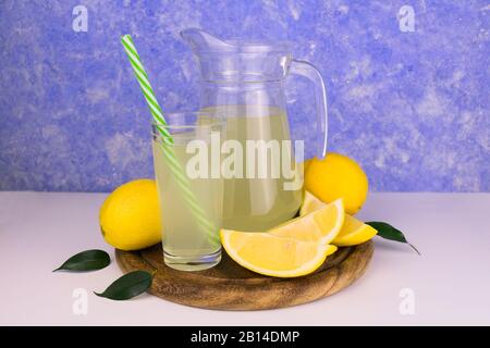 Una bevanda rinfrescante al limone in una brocca e limoni maturi di colore azzurro sul retro Foto Stock