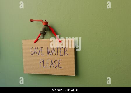 Closeup segno di cartone con scrittura a mano SALVARE L'ACQUA SI PREGA di appendere su vecchio rubinetto installato su parete verde, concetto di conservazione dell'acqua Foto Stock