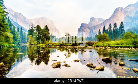 Riflessioni di Cathedral Rocks, Taft Point e Sentinel Dome nel fiume Merced nella valle di Yosemite piena di fumo a causa del fuoco di Briceburg del 2019 ou Foto Stock