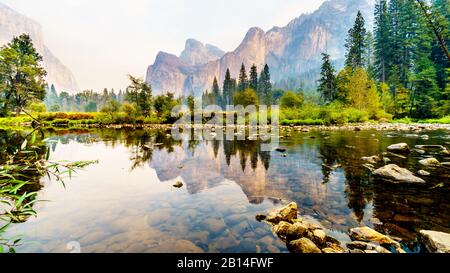 Riflessioni di Cathedral Rocks, Taft Point e Sentinel Dome nel fiume Merced nella valle di Yosemite piena di fumo a causa del fuoco di Briceburg del 2019 ou Foto Stock