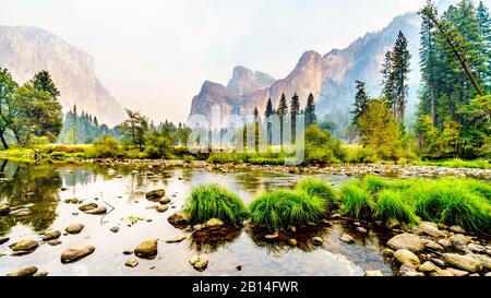 Riflessioni di Cathedral Rocks, Taft Point e Sentinel Dome nel fiume Merced nella valle di Yosemite piena di fumo a causa del fuoco di Briceburg del 2019 ou Foto Stock