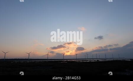 Tramonto di sole in serata, con silhouette di turbine eoliche all'orizzonte lontano. Foto Stock