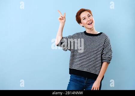 Ragazza allegra con i capelli corti dello zenzero che fa i gesti con la sua mano Foto Stock