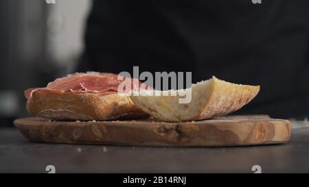 l'uomo aggiunge il prosciutto sulla ciabatta a bordo di olive, foto larga Foto Stock