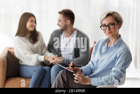 Lo Psicologo Di Famiglia Sorridente Mentre La Coppia Che Si Riconciliano Seduto Sul Divano Interno Foto Stock