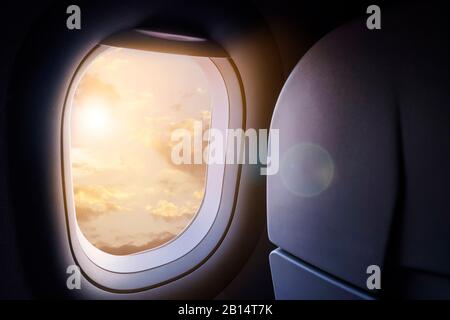 Nuvole e cielo con luce solare dorata e riflessi lenti come si vede attraverso la finestra di un aereo Foto Stock