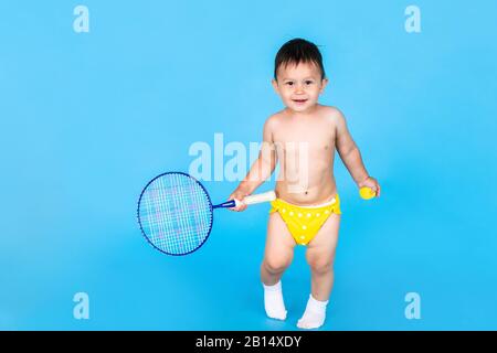 Adorabile ragazzino che gioca a badminton sullo sfondo blu. Attività estive per bambini. Foto Stock