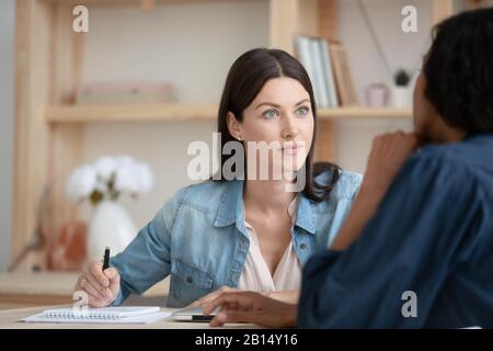 Attento giovane donna dipendente della compagnia che ascolta il cliente americano africano. Foto Stock