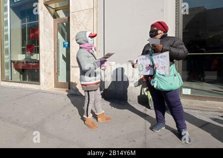 Due donne americane di mezza età che indossano maschere chirurgiche distribuiscono volantini pubblicitari in una giornata invernale frigid. A Chinatown, Flushing, Queens, Nyc Foto Stock