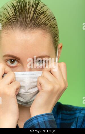 giovane donna in maschera di protezione medica guardando la fotocamera su sfondo verde Foto Stock