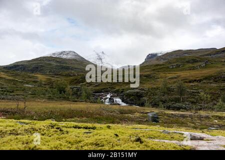 Montagna pittoresca vista con neve, cascata, rocce, muschio verde, alte cime Norvegia autunno paesaggio viaggio Norvegia, epiche nuvole in Tindevegen Foto Stock